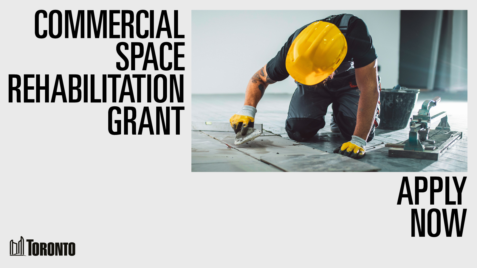 Construction worker wearing a yellow hard hat kneeling on the group while laying tiles on the ground